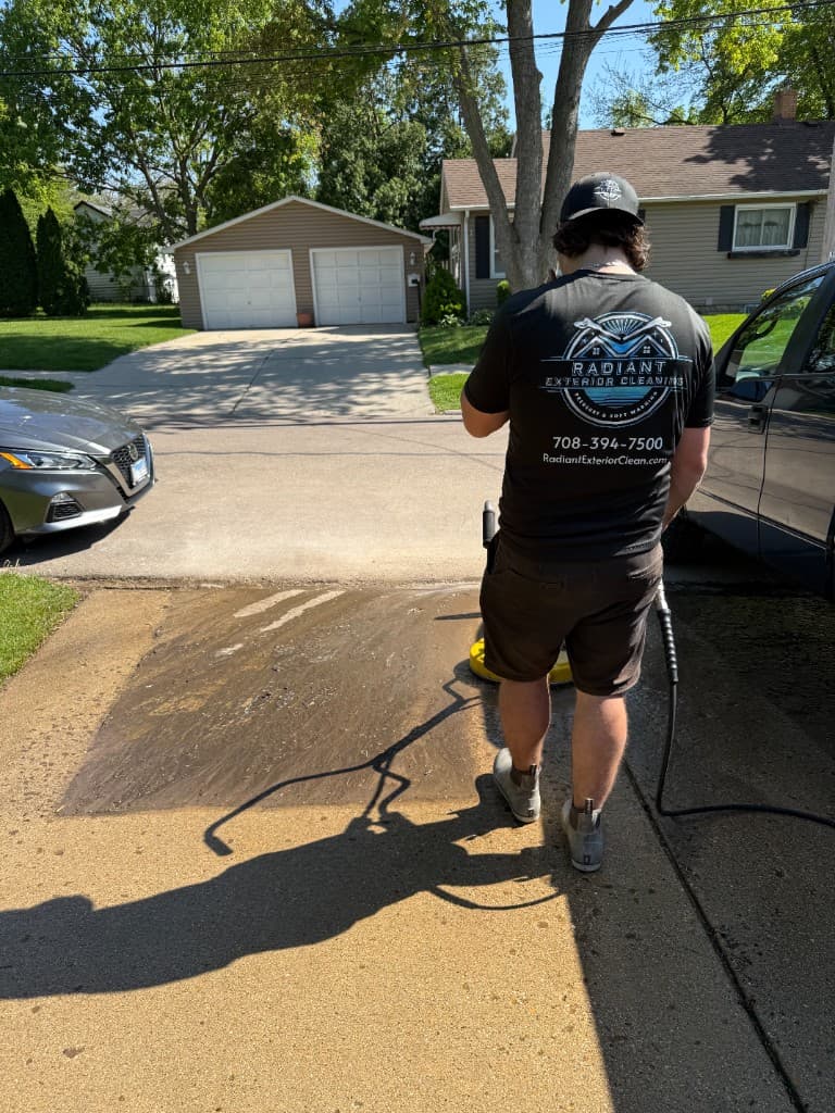 Radiant Exterior Cleaning technician using a professional surface cleaner on a residential concrete driveway, branded uniform