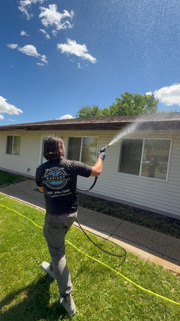 Radiant Exterior Cleaning pressure washing upper siding and trim on a Florida home, in uniform